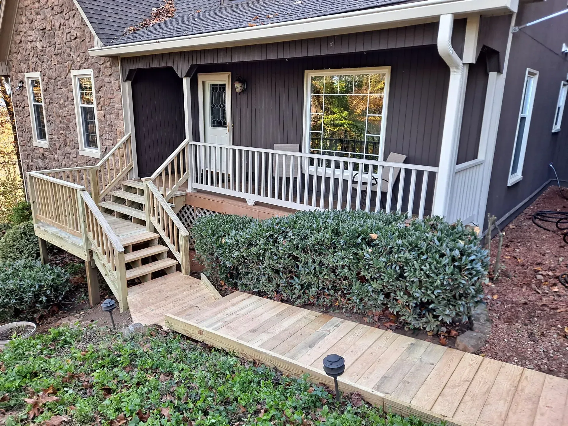 Wooden ramp and stairs leading to a house with brown siding, white trim, and green bushes.
