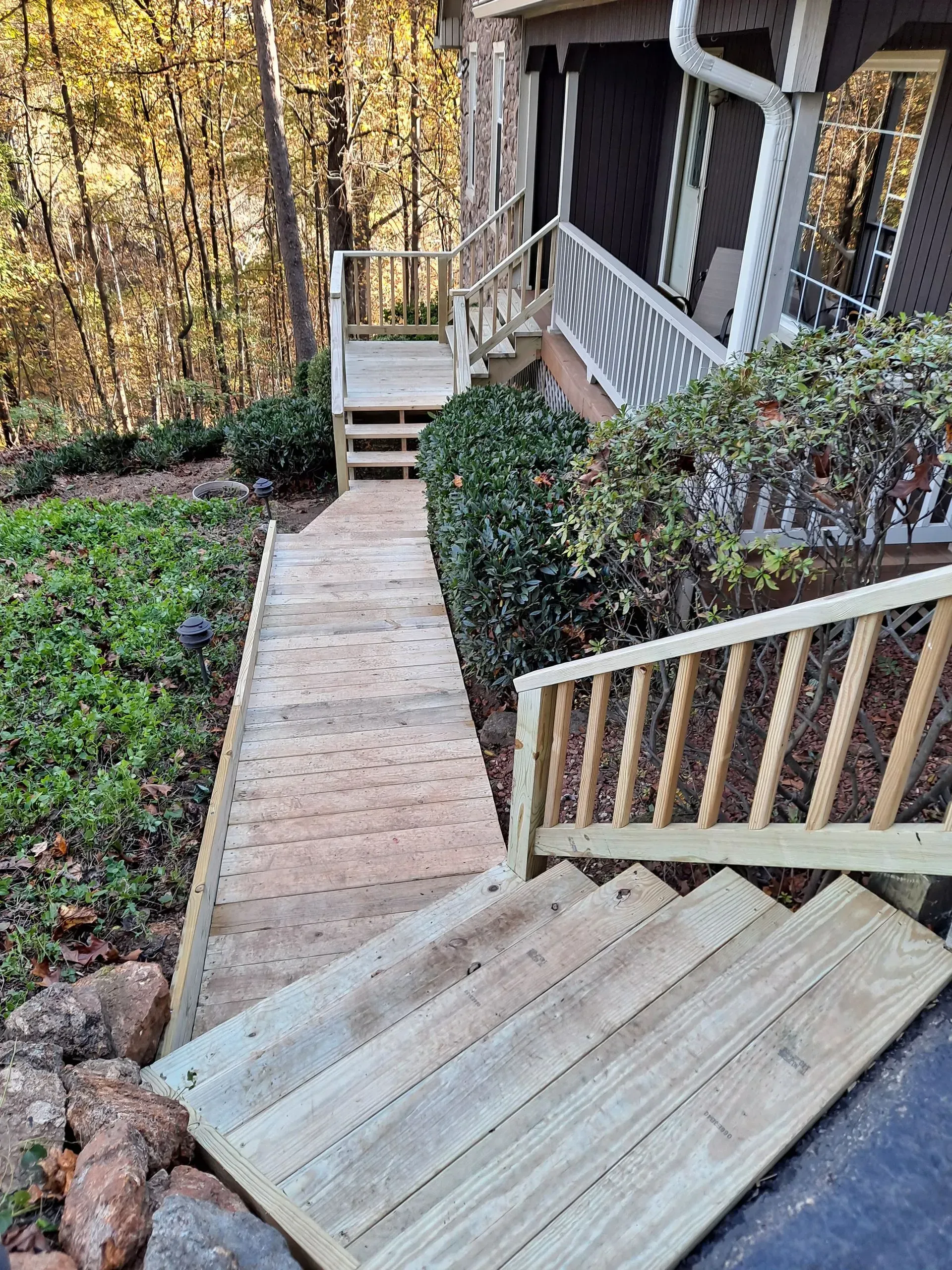 A wooden ramp and stairs lead up to a house with a forest background.