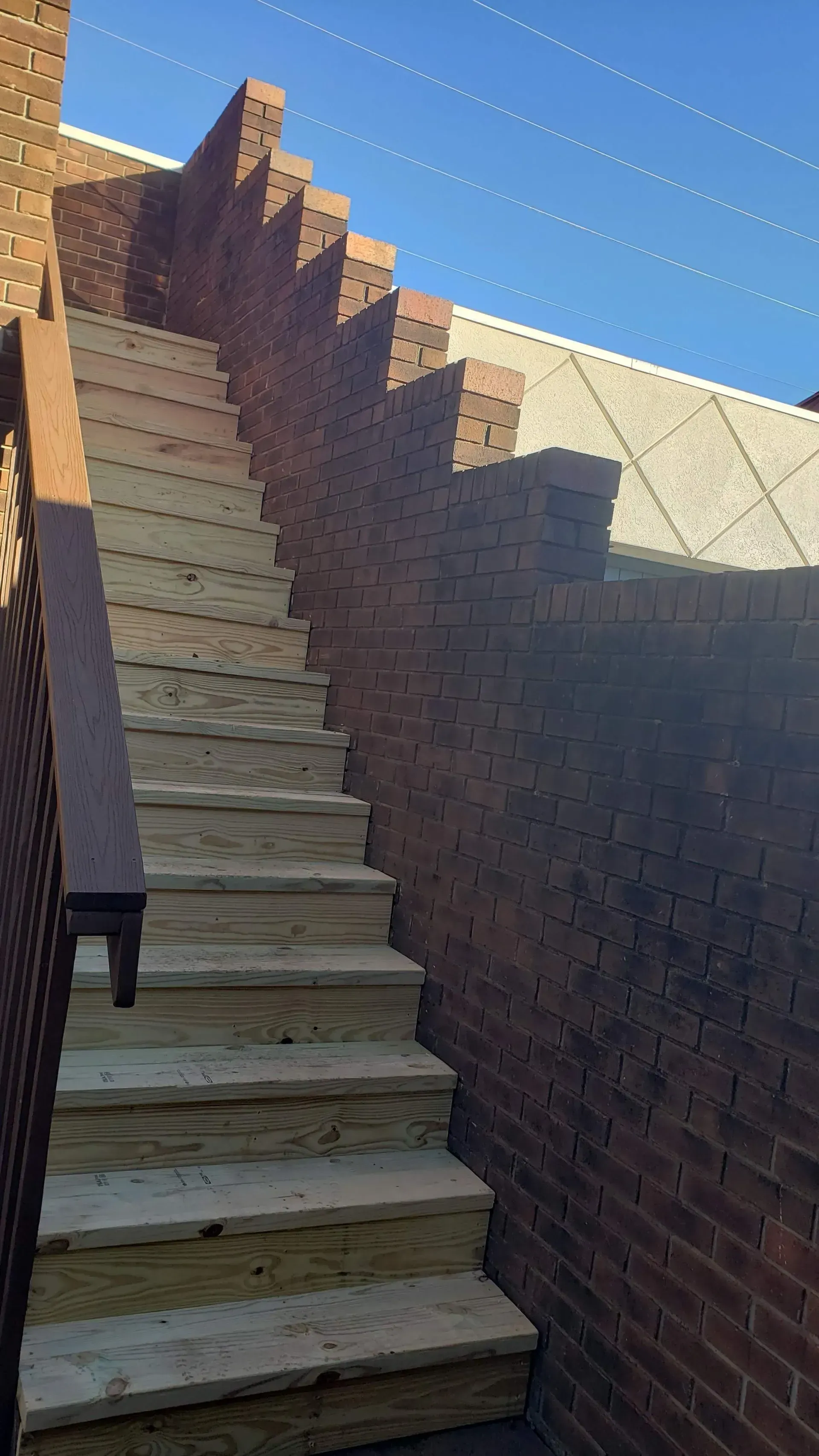 Brick staircase with wooden steps, ascending between brick walls and a metal roof.
