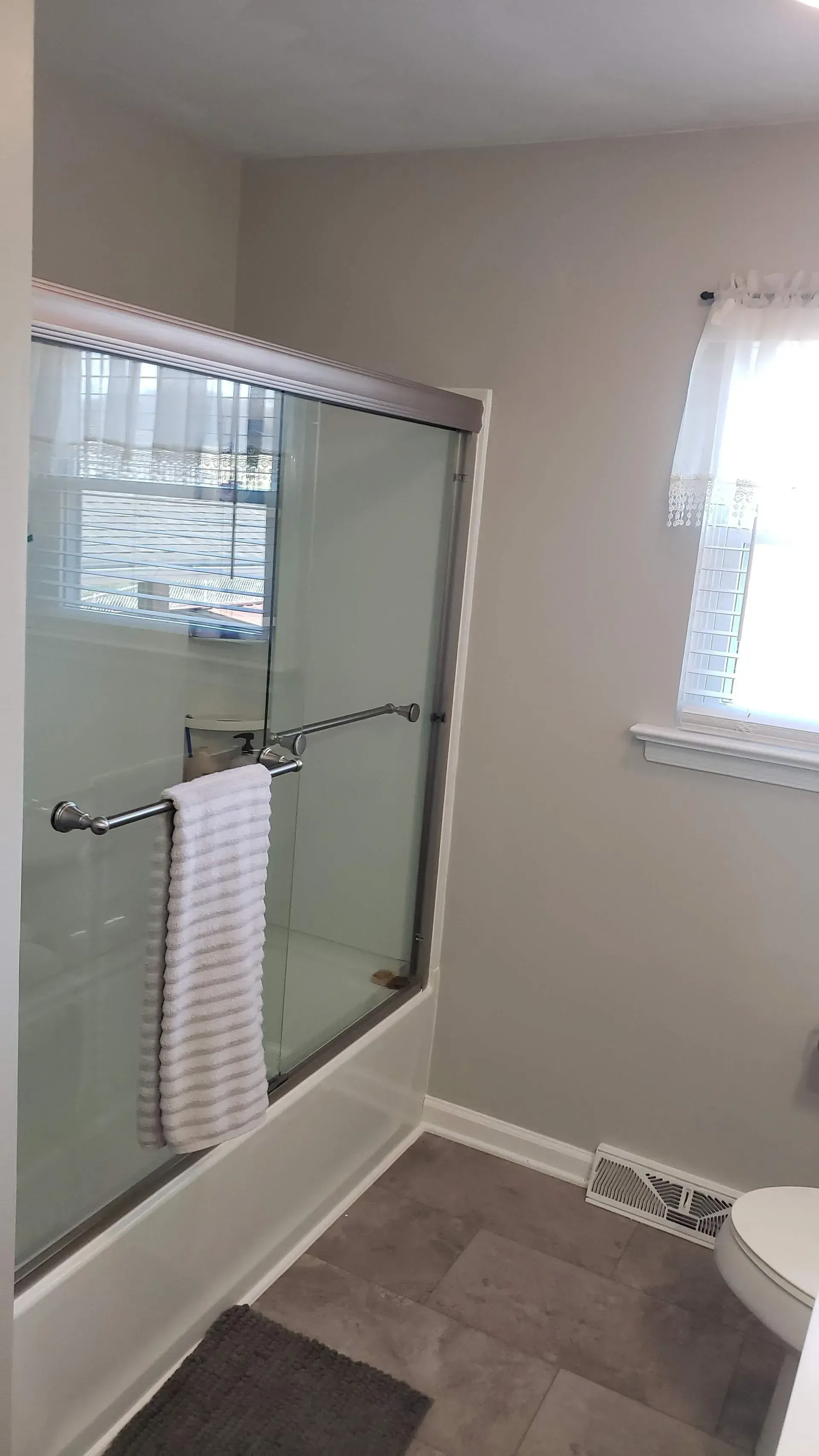 Bathroom with a shower behind a glass door, a window, and a towel hanging on the door.