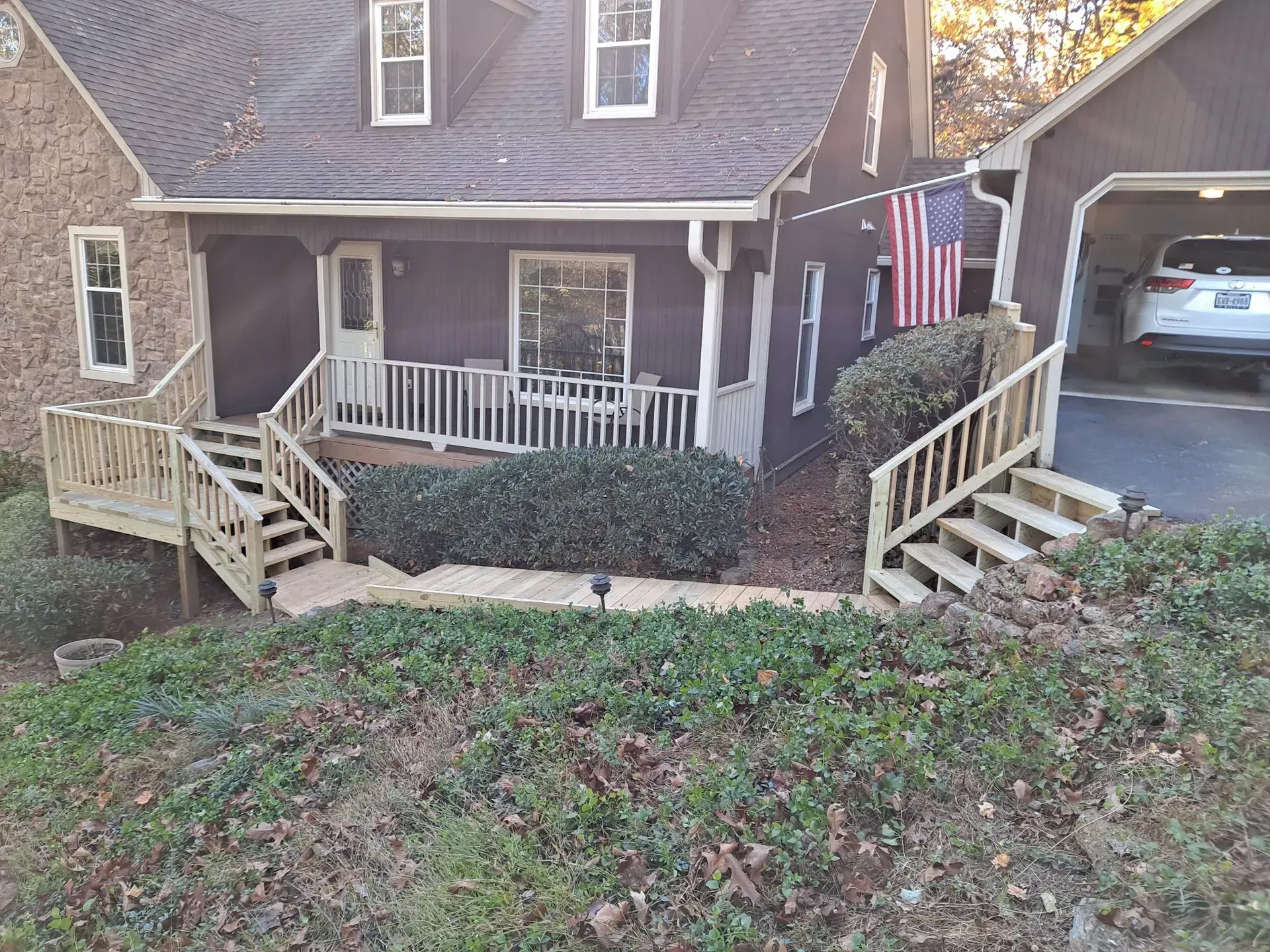 Two-story dark house with steps, porch, and garage. American flag hangs near the garage.