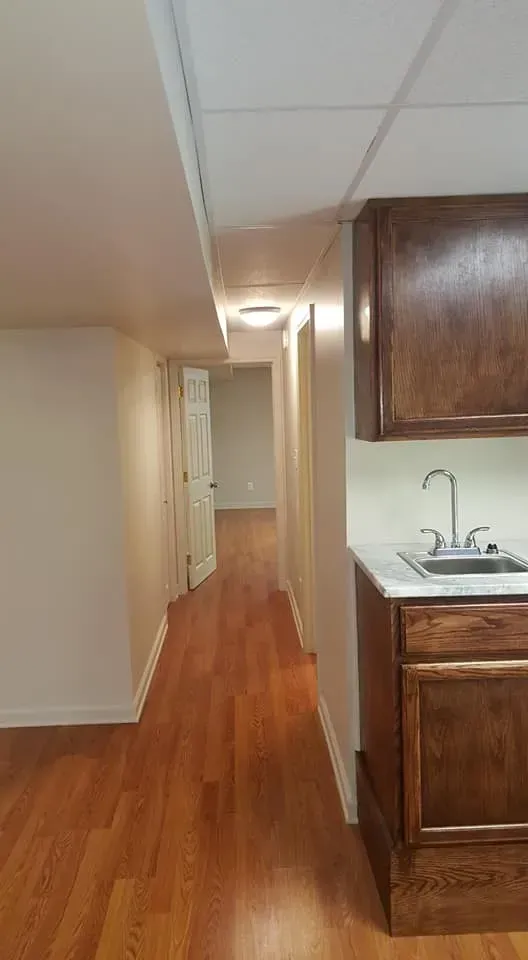Long hallway with wood flooring, white walls, and a small sink.