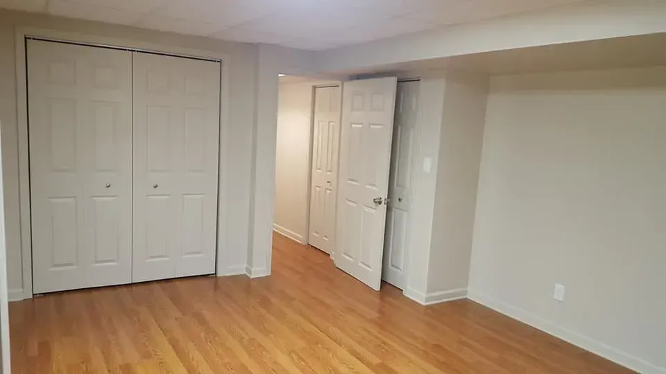 A small empty room with light brown wood floors, a large closet, and two other doorways.