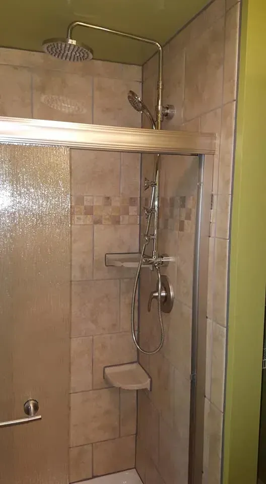 Shower with beige tile walls, gold shower head, and a built-in seat.