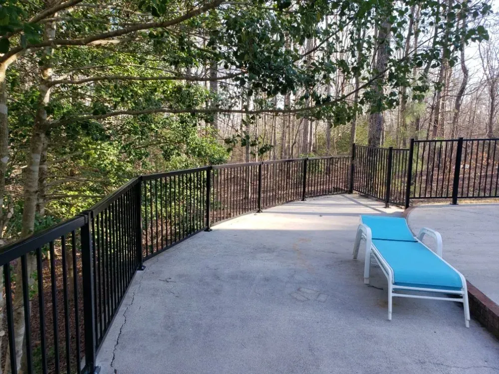 Black railing curves around a concrete patio with a lounge chair, trees in the background.