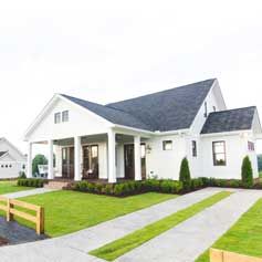A white house with a black roof is sitting on top of a lush green lawn.