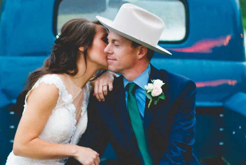 A bride and groom are kissing in front of a blue truck.