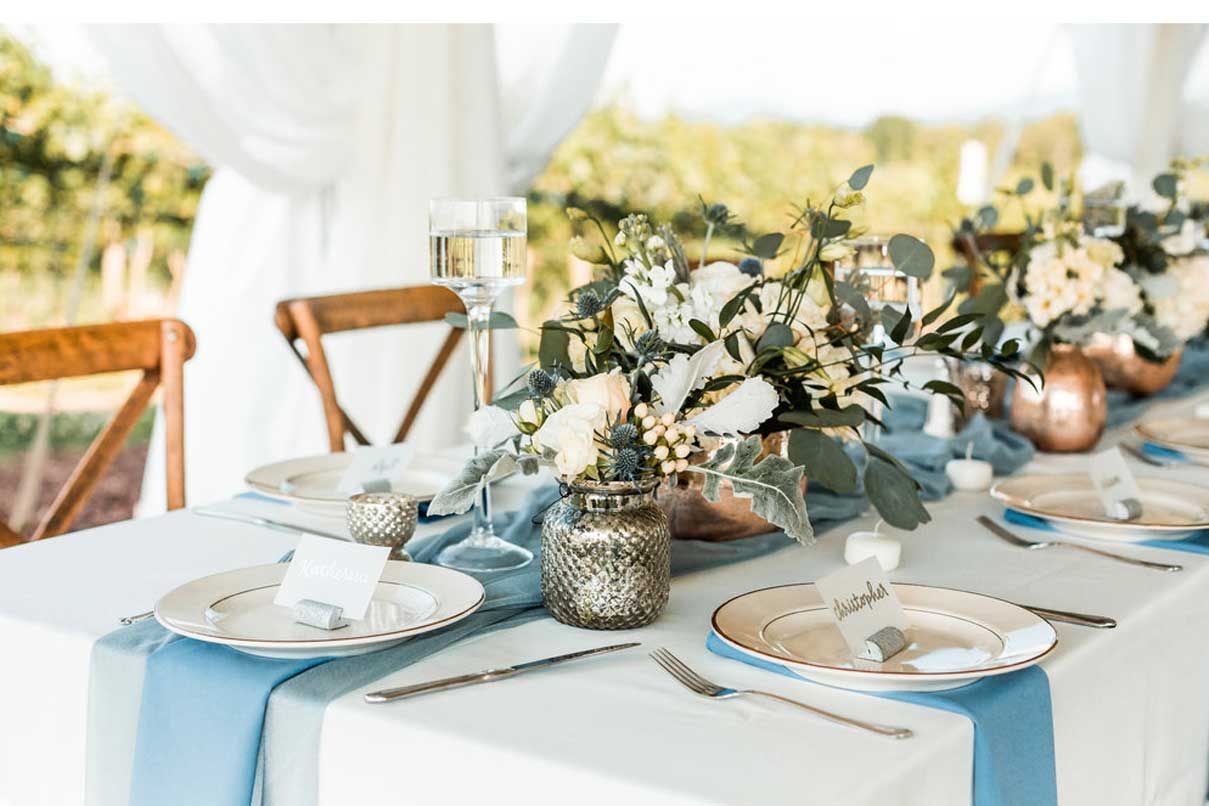 A long table with plates , silverware , and a vase of flowers on it.