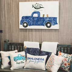 A couch with pillows and a painting of a blue truck on the wall.