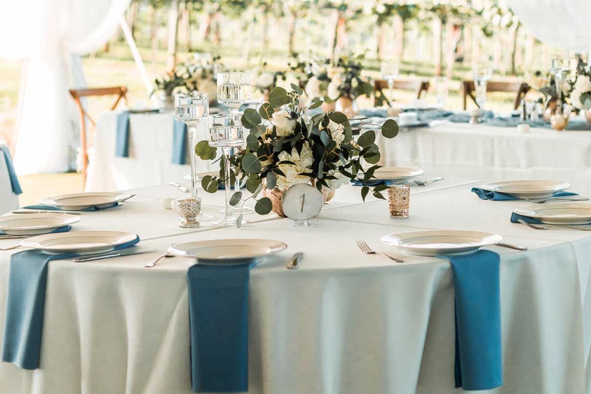 A table set for a wedding reception with blue napkins and plates.