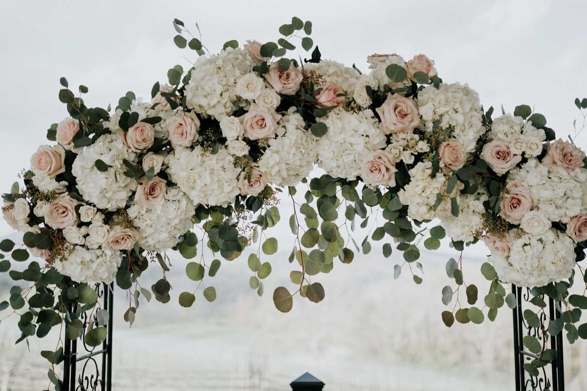 A wedding arch decorated with white flowers and green leaves.