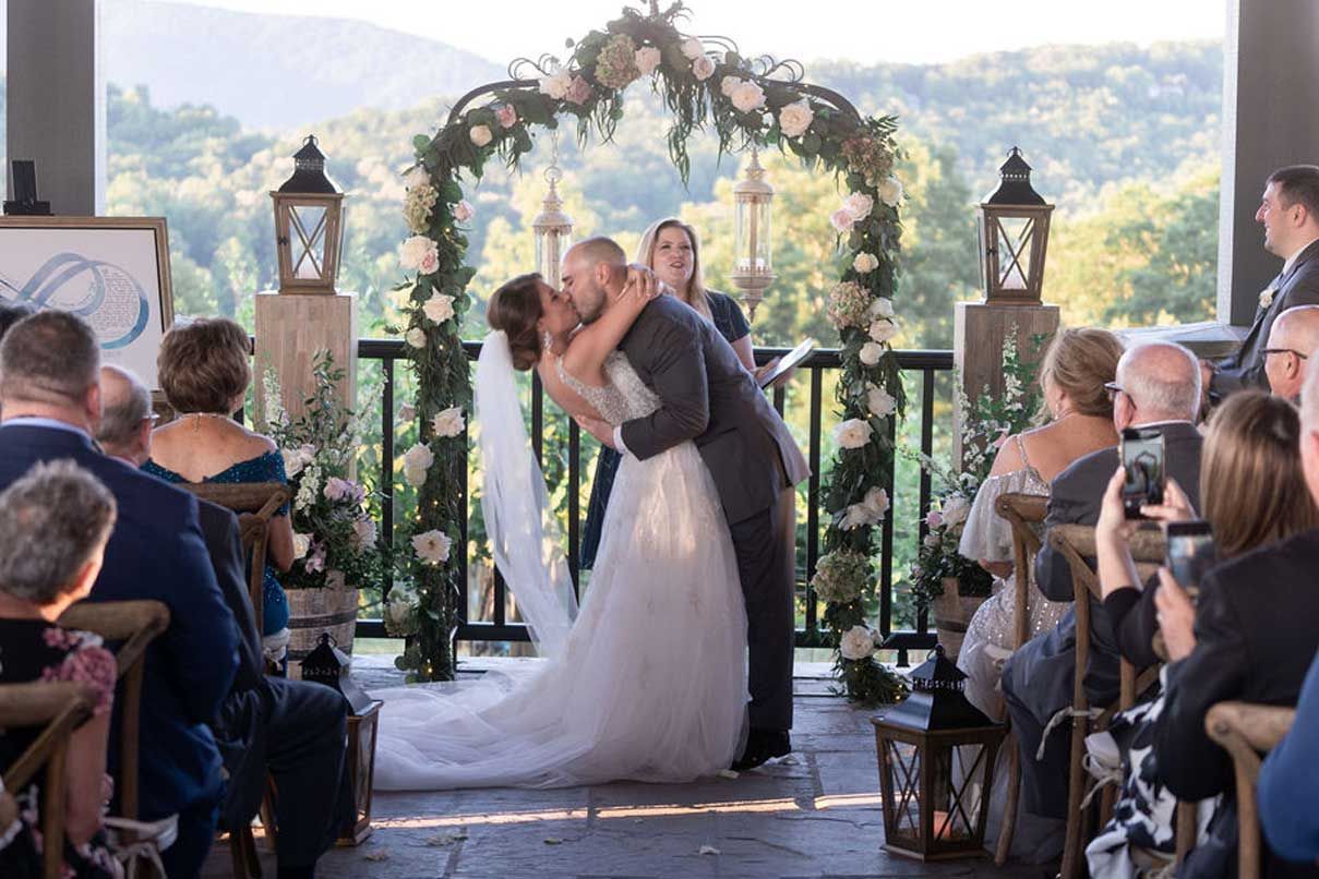 A bride and groom kissing at their wedding ceremony while their guests watch.