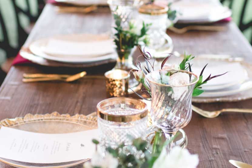 A wooden table with plates , glasses , silverware and flowers on it.