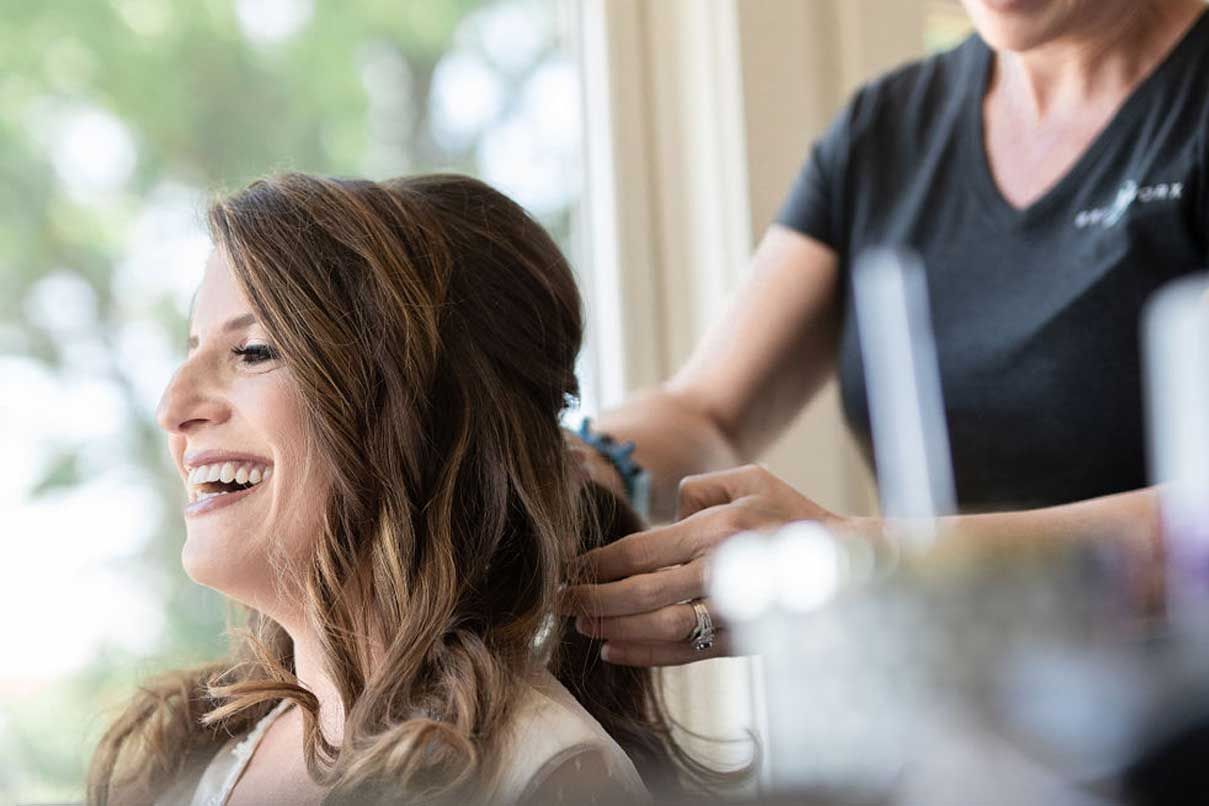 A woman is getting her hair done by a hairdresser in front of a window.