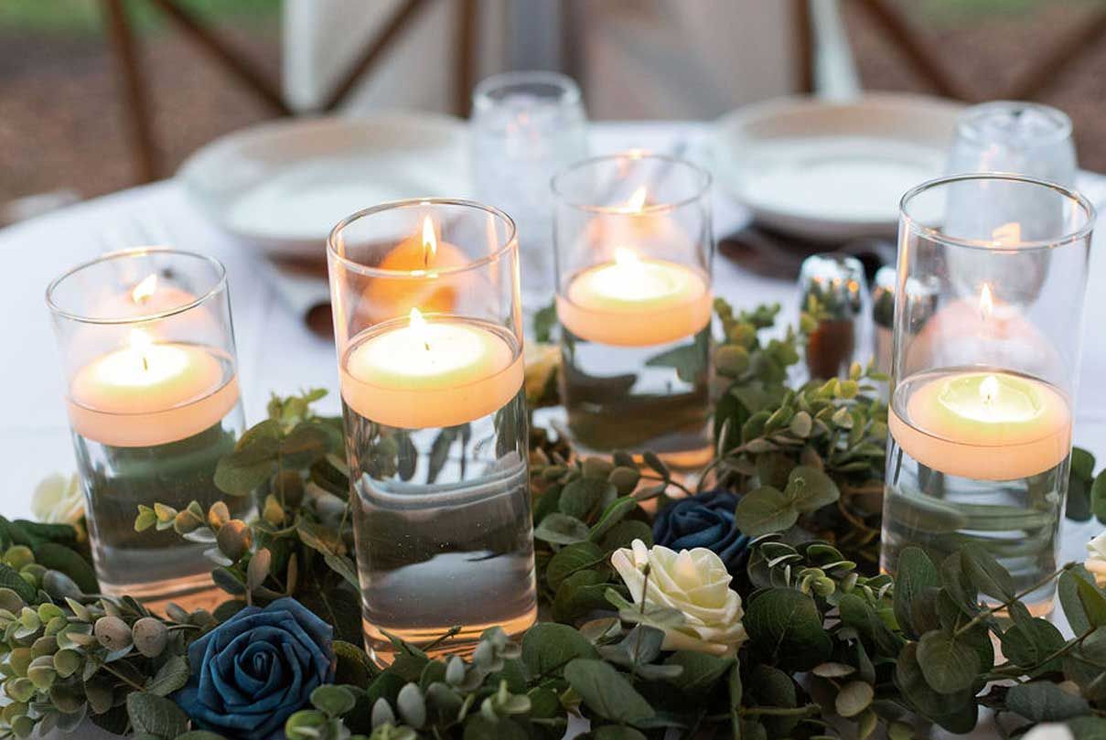 A table with candles in glasses and flowers on it.