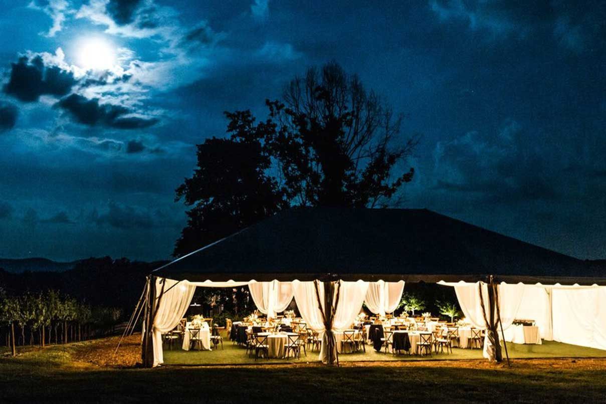 A tent is lit up at night with a full moon in the background.