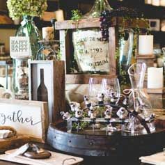 A table topped with bottles , glasses , candles and a sign that says `` gather ''.