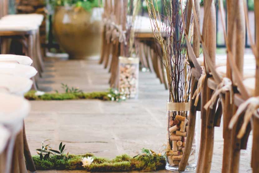 A row of wooden chairs with flowers in vases on the floor.