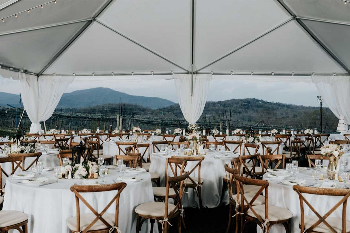 A tent with tables and chairs set up for a wedding reception with mountains in the background.