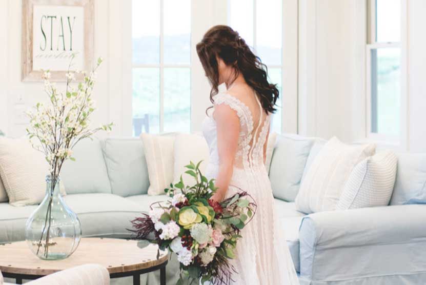 A bride in a wedding dress is holding a bouquet of flowers in a living room.