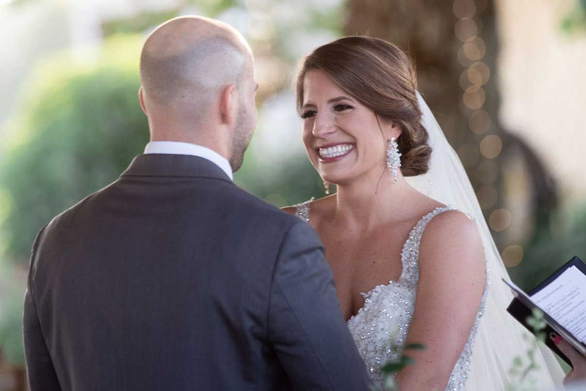 A bride and groom are smiling at each other during their wedding ceremony.