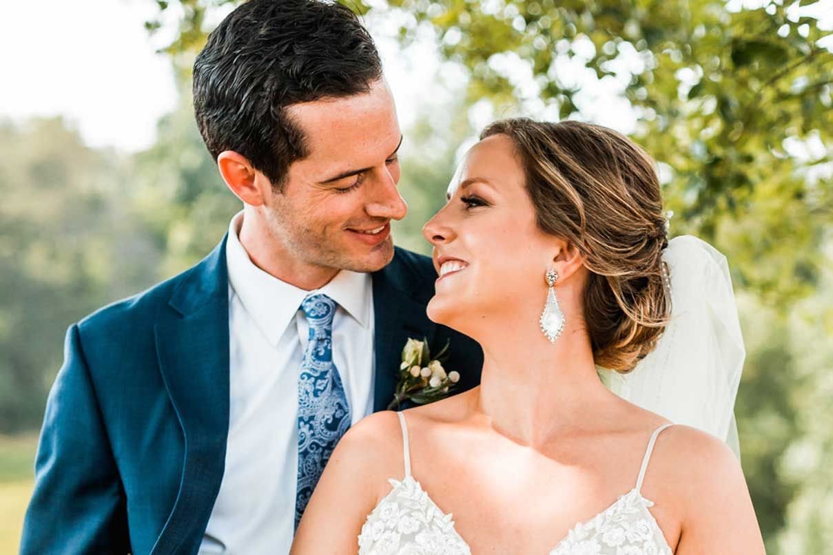 A bride and groom are posing for a picture under a tree on their wedding day.