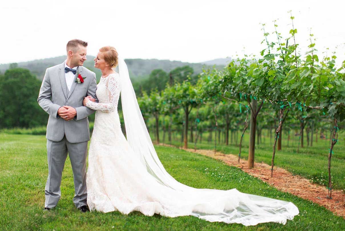 A bride and groom are standing next to each other in a vineyard.