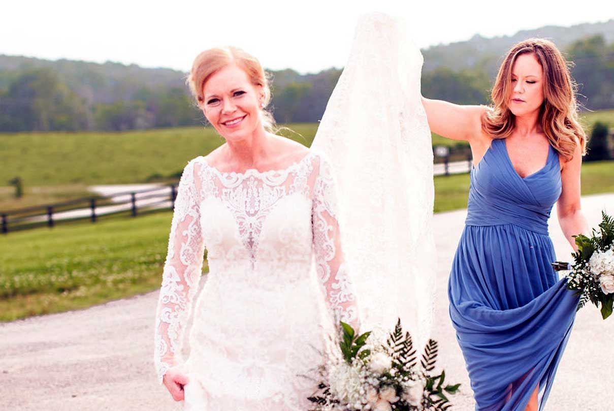 A bride and her bridesmaid are standing next to each other holding their wedding dresses.