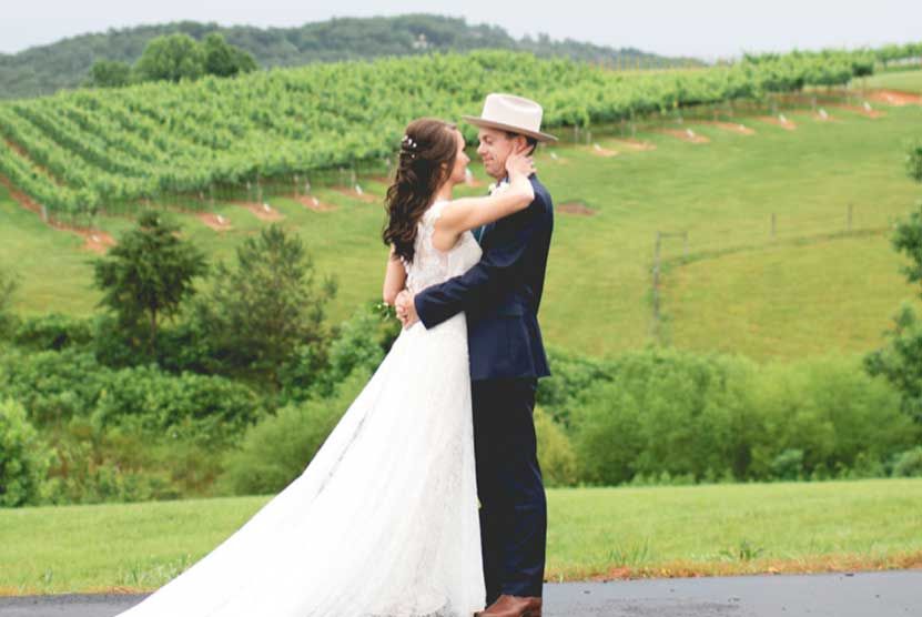 A bride and groom are posing for a picture in front of a vineyard.