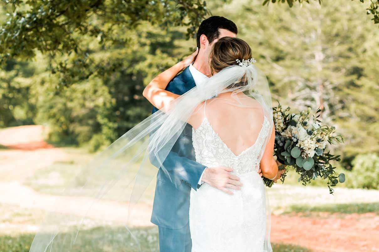 A bride and groom are kissing under a tree on their wedding day.