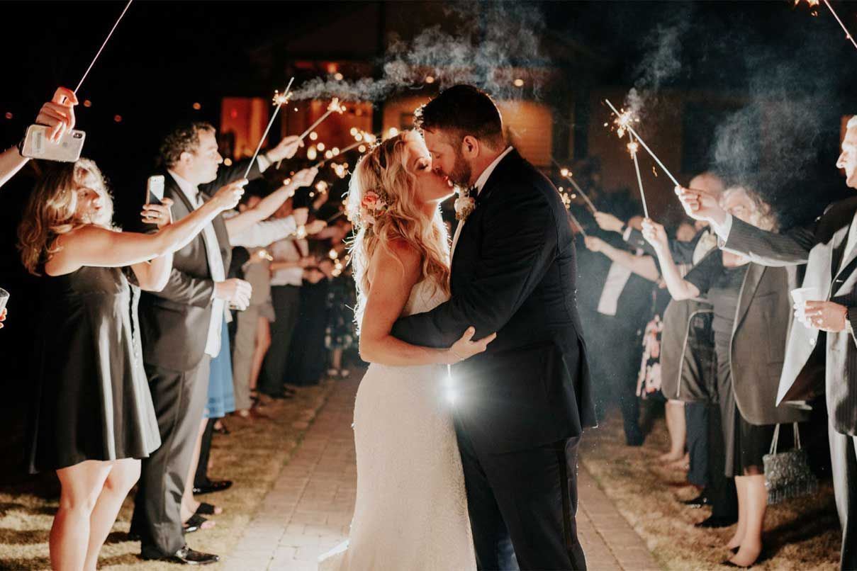 A bride and groom kissing in front of a crowd of people holding sparklers.