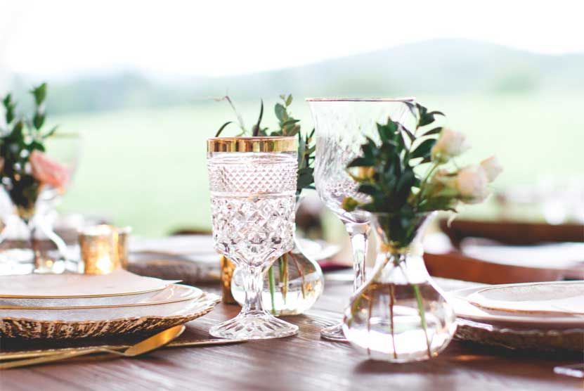 A table with plates , glasses , vases and flowers on it.