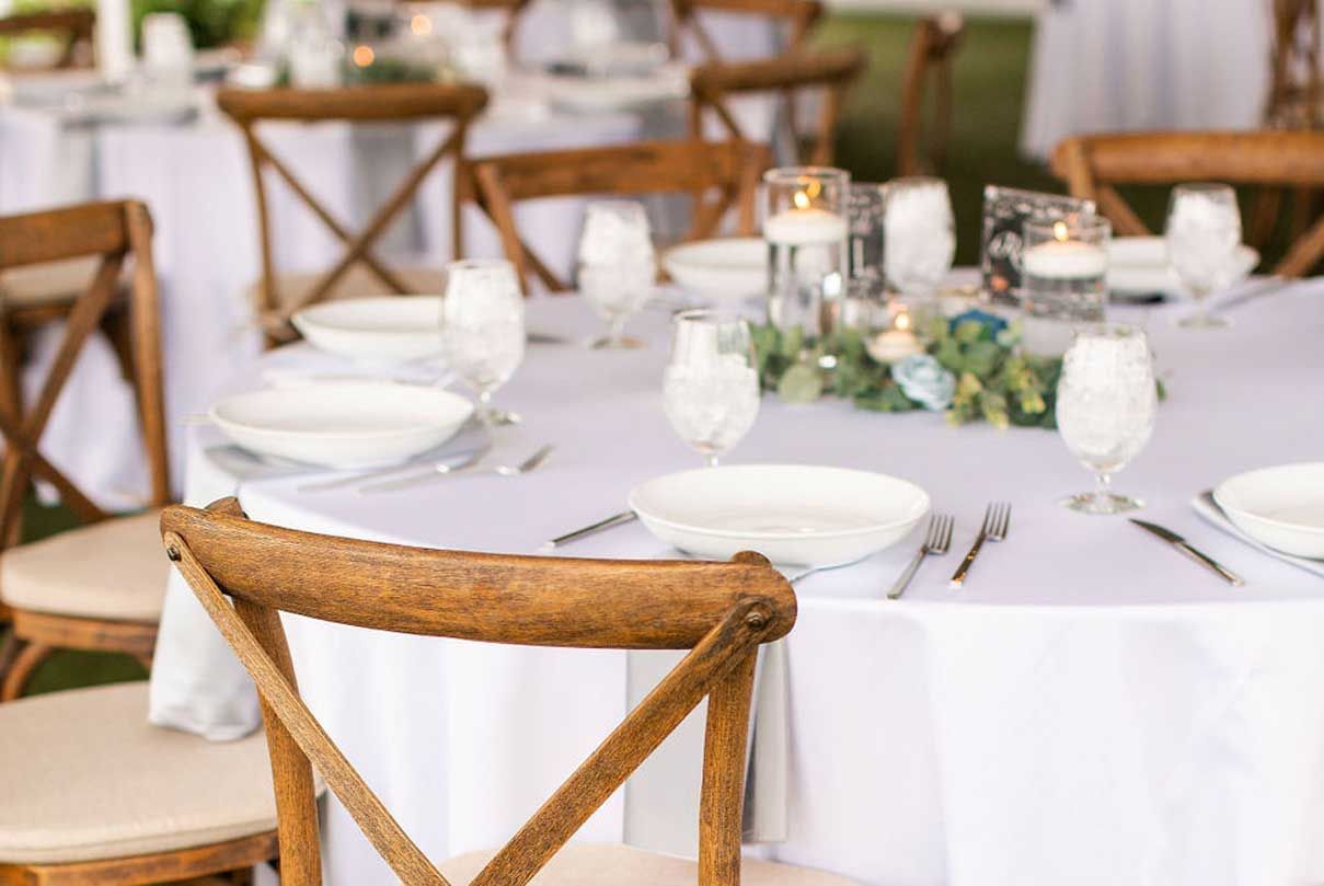 A wooden chair is sitting in front of a table set for a wedding reception.