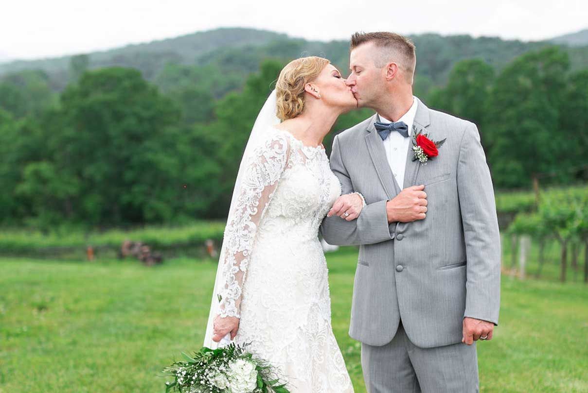A bride and groom are kissing in a field.