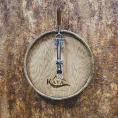 A wooden barrel with a corkscrew on it is hanging on a wall.