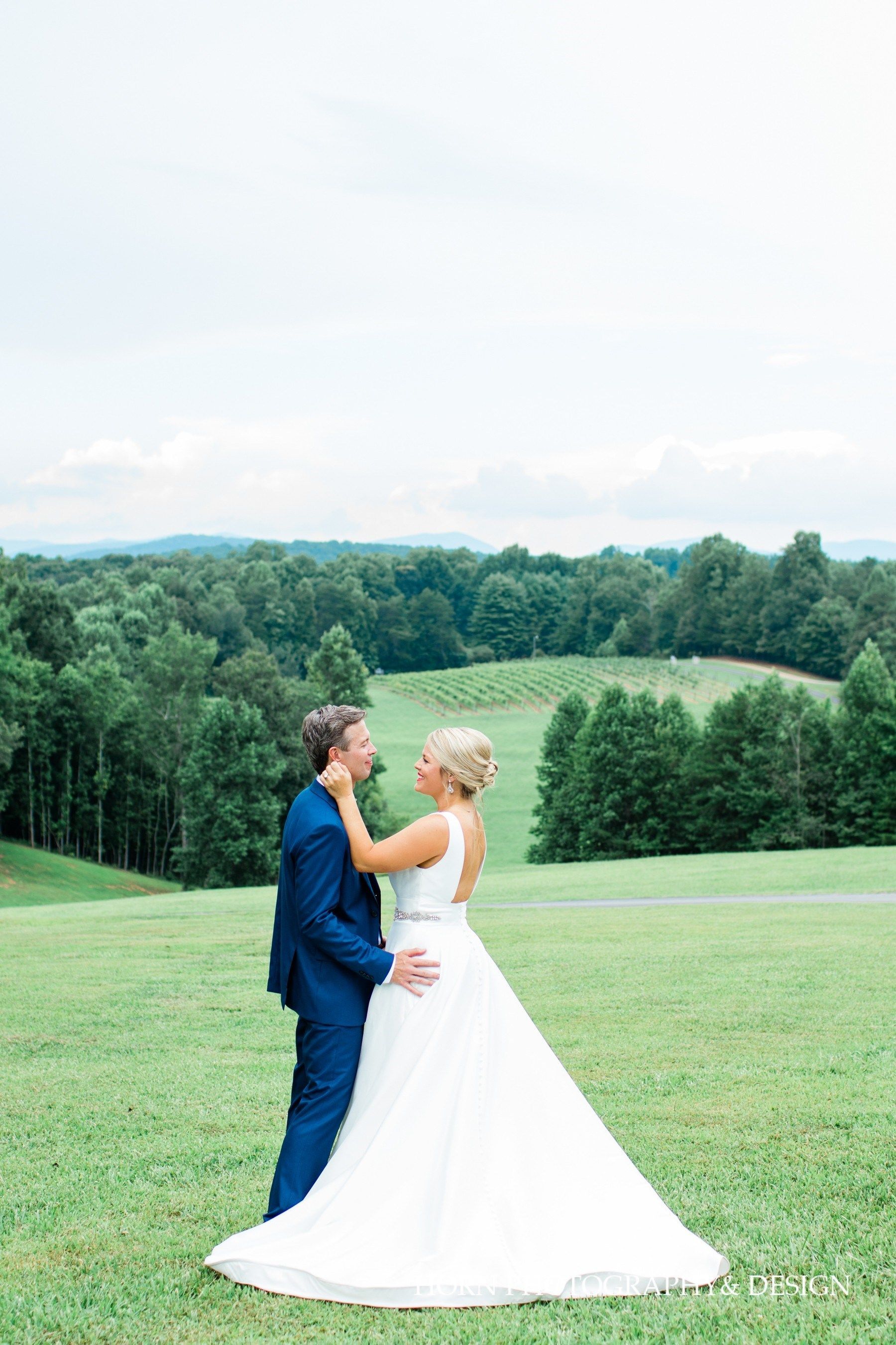 A bride and groom are standing in a grassy field looking at each other.