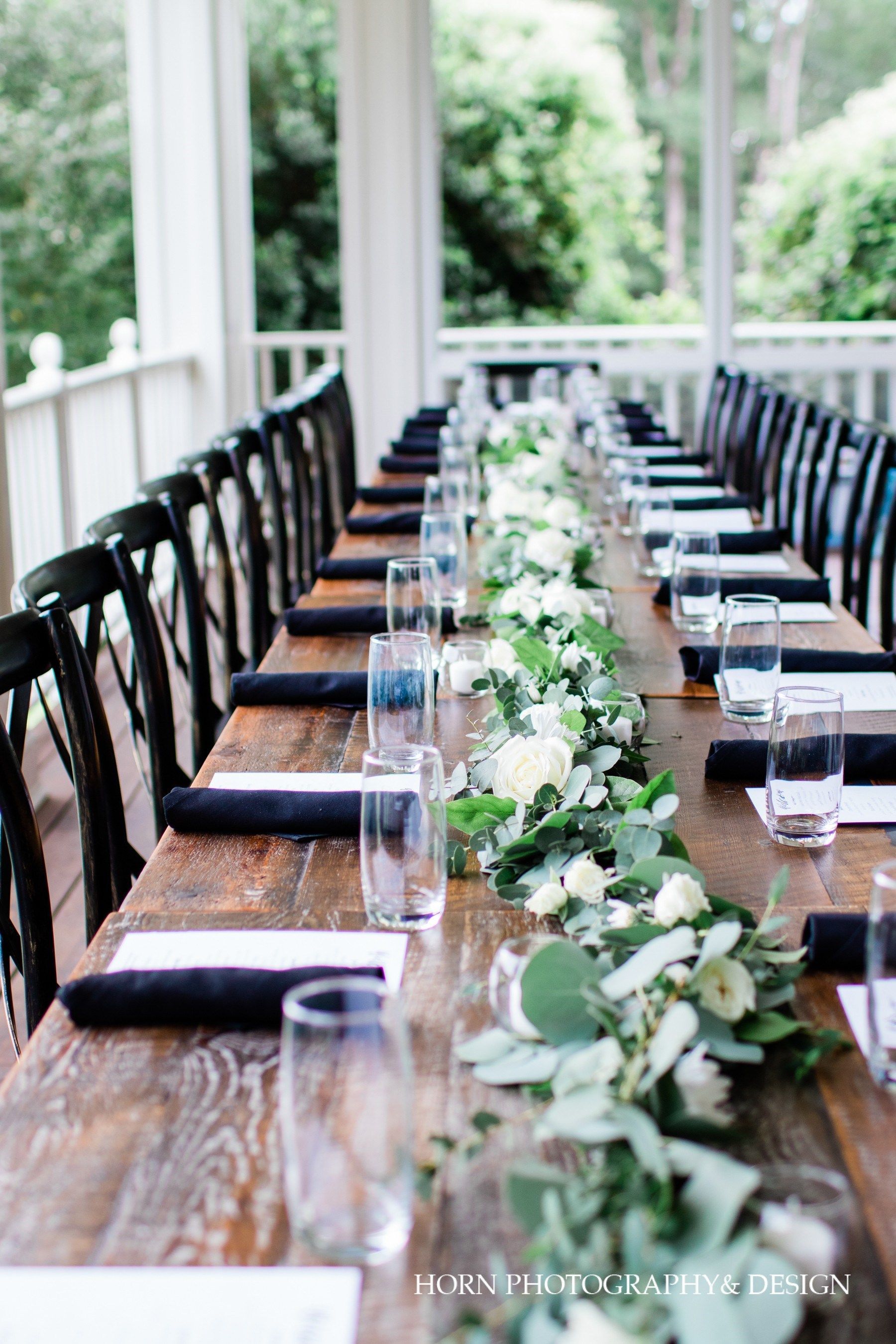 A long wooden table with glasses , napkins , and flowers on it.