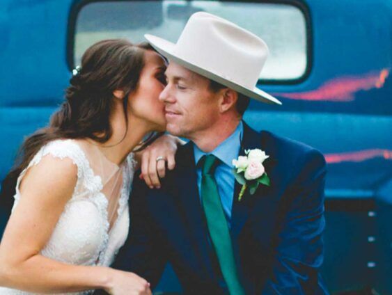 A bride and groom are kissing in front of a blue truck.