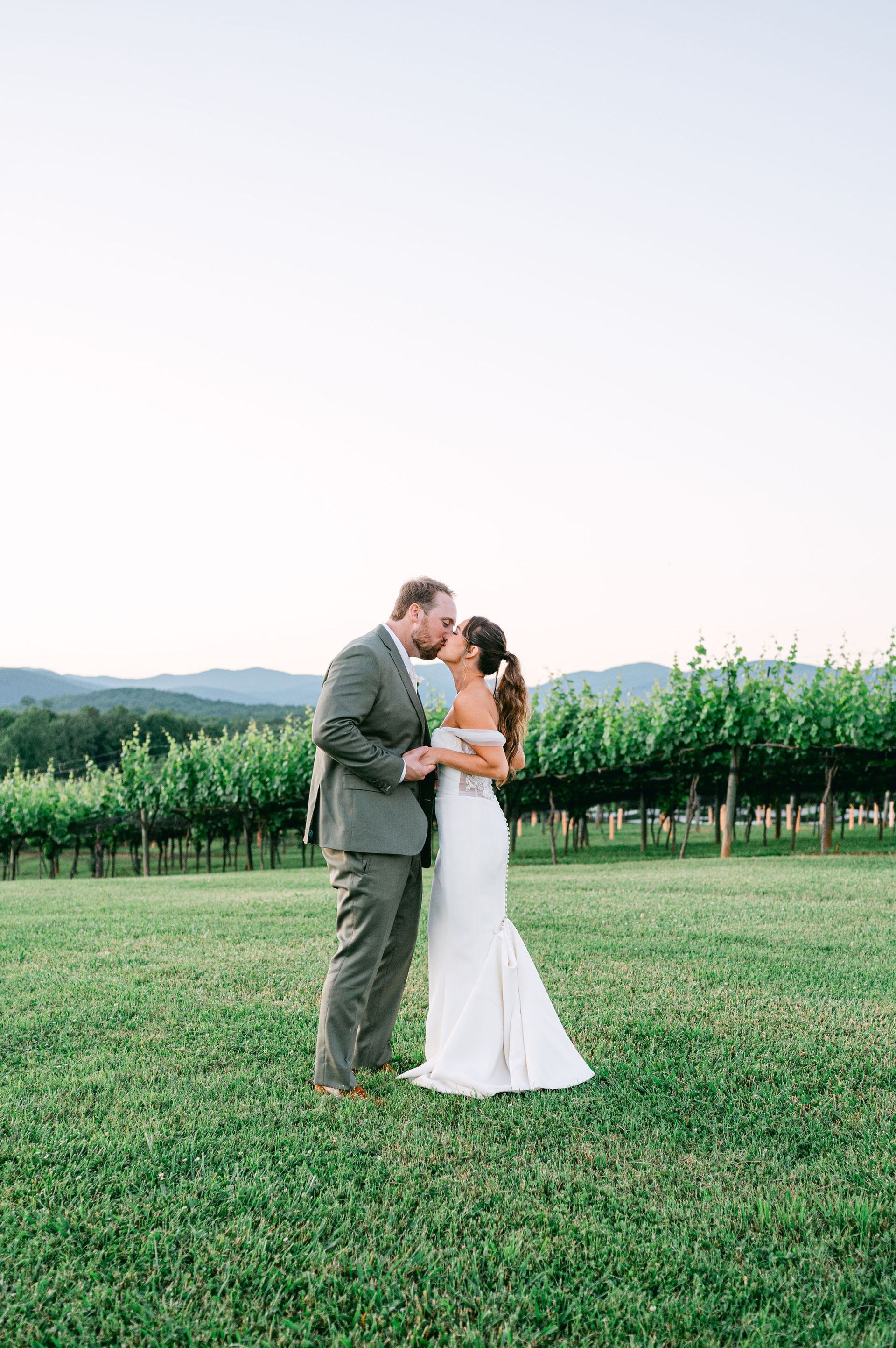 A bride and groom are standing in a grassy field looking at each other.