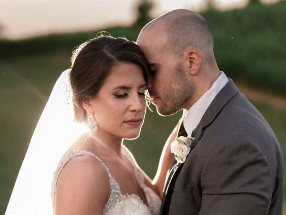 A bride and groom are posing for a picture and the groom is kissing the bride on the forehead.