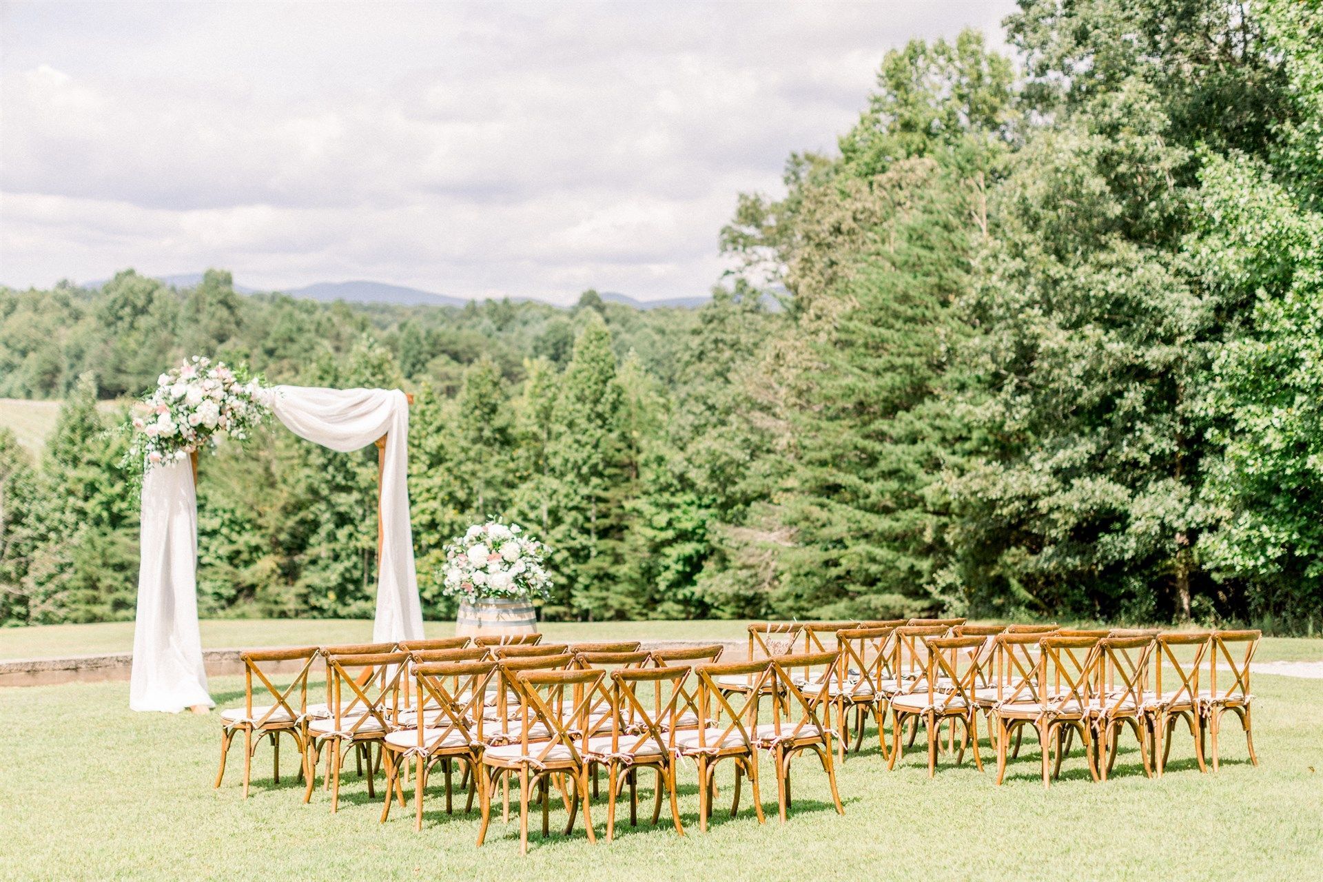 A row of wooden chairs are lined up in a field for a wedding ceremony.