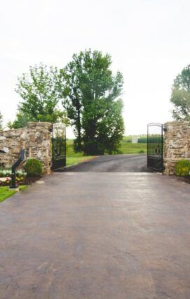 A driveway with a stone wall and a gate