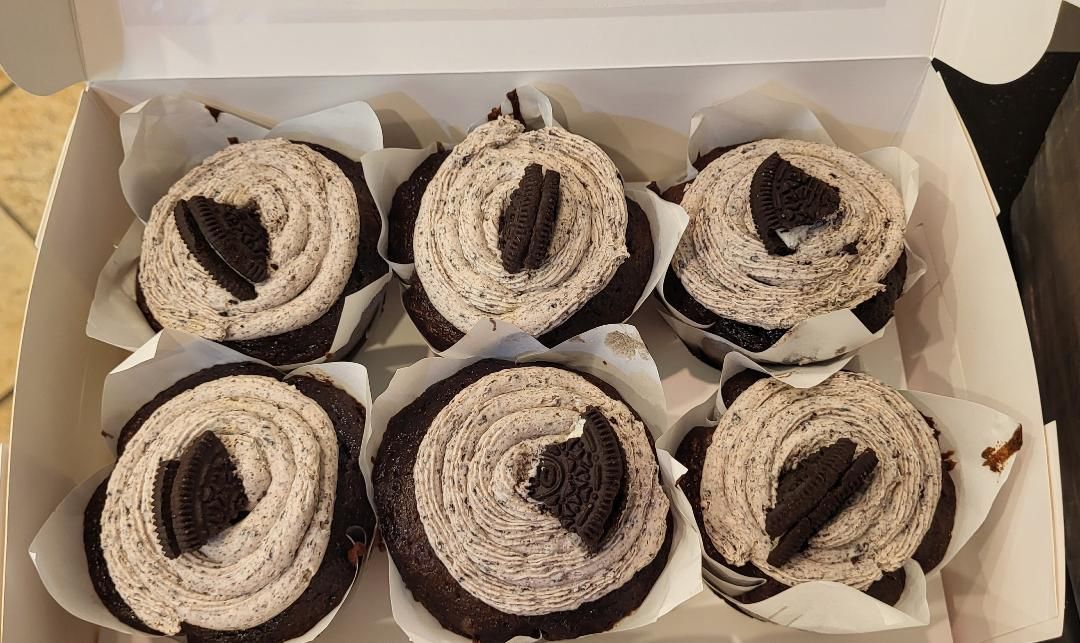 Pink frosted cupcakes with white sprinkles in a display case.