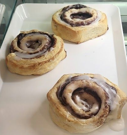 Two boxes of pastries, including strawberry and peach danishes, donuts, and a brownie, on a counter.