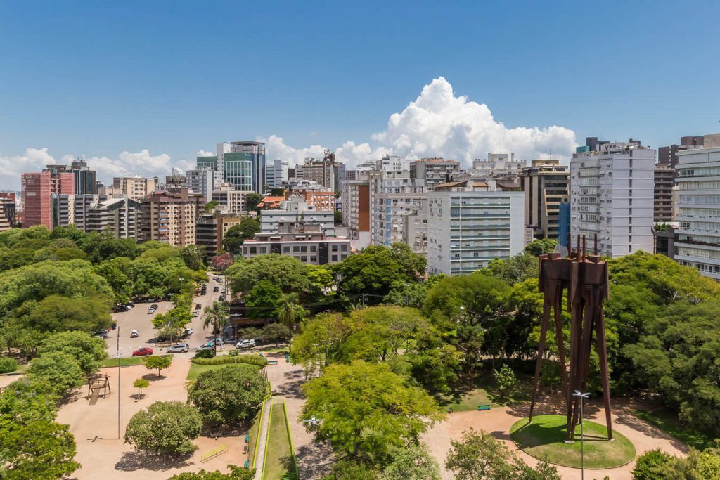 Uma vista aérea de uma cidade com um parque em primeiro plano e uma estátua ao fundo.