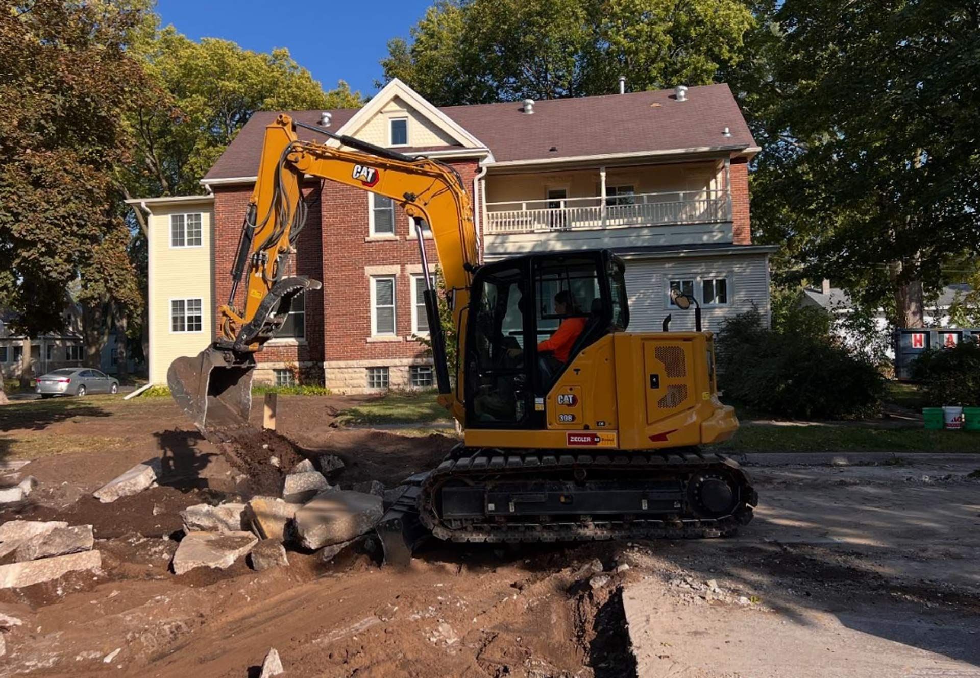 A yellow excavator is moving rocks in front of a brick house