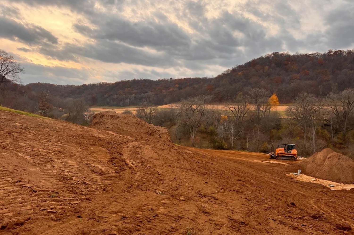 A bulldozer is driving down a dirt road with mountains in the background.