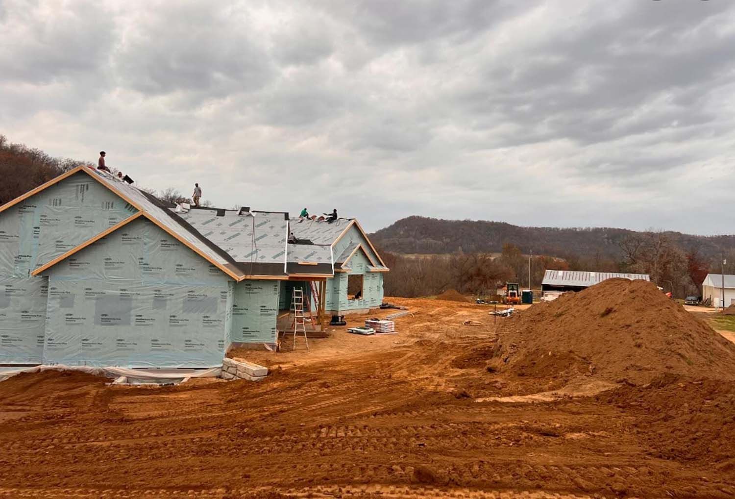 A house is being built in a dirt field next to a pile of dirt.