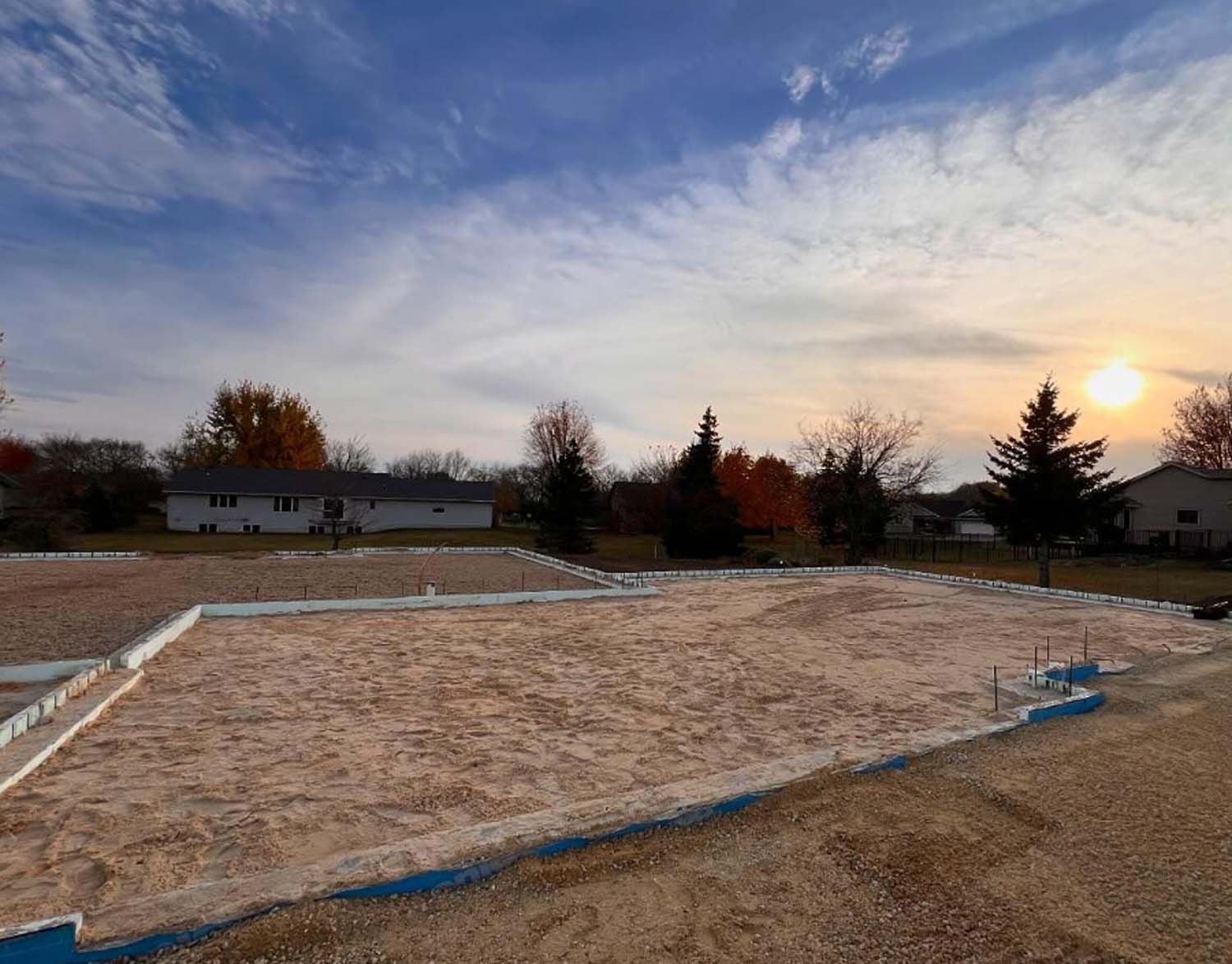 The sun is setting over a dirt field with a house in the background.