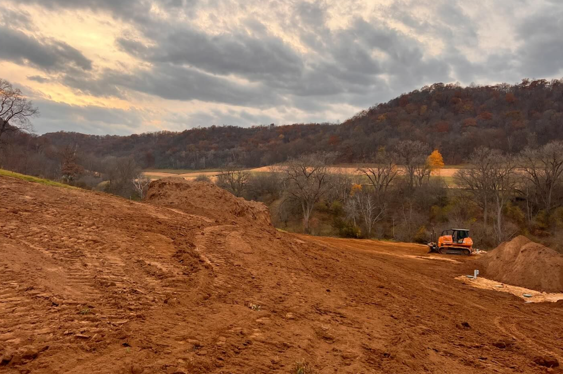 A truck is driving down a dirt road with mountains in the background.